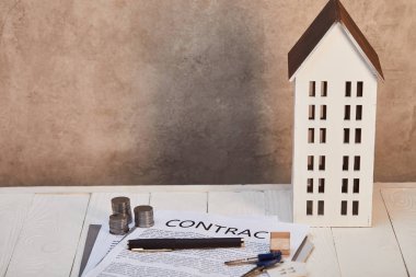 Beyaz ahşap masa üzerinde ev modeli sözleşme, sikke ve kahverengi duvar, gayrimenkul kavramı yakın tuşları