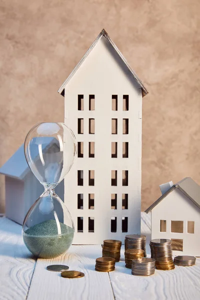 Houses Models Coins Hourglass White Wooden Table Textured Wall Real — Stock Photo, Image