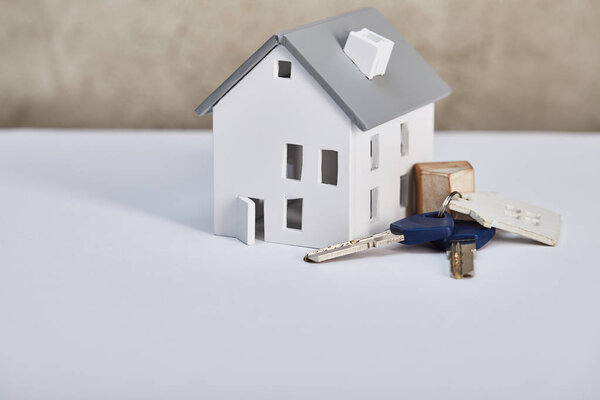 house model on white table with keys near grey textured wall, real estate concept