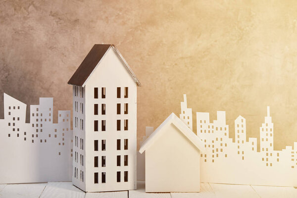 houses models on white wooden table near white paper cut city in sunlight, real estate concept