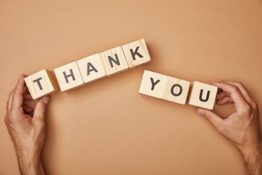 cropped view of man holding wooden cubes with thank you lettering on beige background clipart