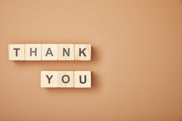 Top view of wooden cubes with thank you lettering on beige background with copy space