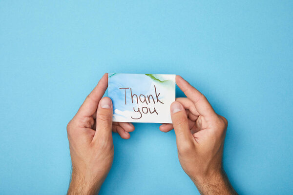 partial view of man holding greeting card with thank you lettering on blue background