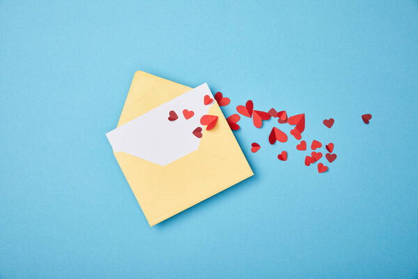 yellow envelope with blank white card and paper cut hearts on blue background