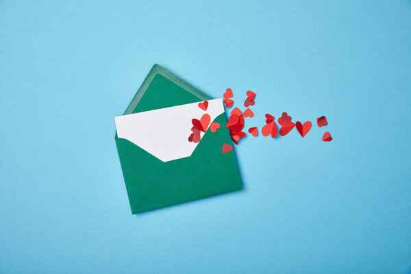 green envelope with blank white card and red paper hearts on blue background