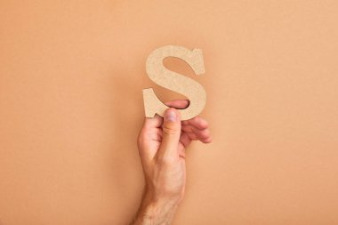 partial view of man holding paper cut letter S on beige background clipart
