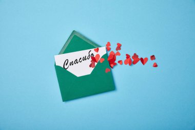 green envelope with thanks lettering in Russian on white card and red paper hearts on blue background clipart
