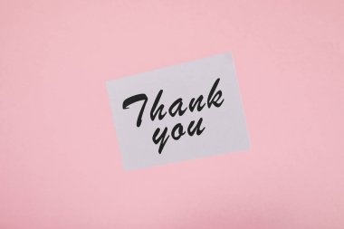 top view of white card with thank you inscription on pink background clipart