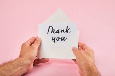 cropped view of man holding envelope and white card with thank you words on pink background clipart