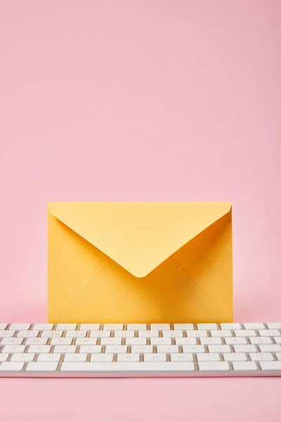 粉红色背景上靠近电脑键盘的黄色信封 — 图库照片