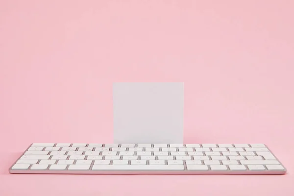 blank white card near computer keyboard on pink background