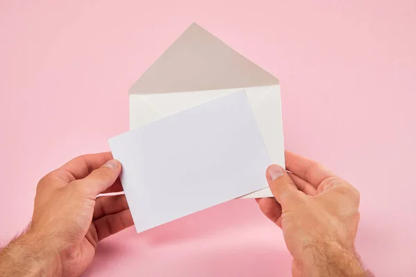 男子拿着信封和空白白卡在粉红色背景的裁剪视图 — 图库照片
