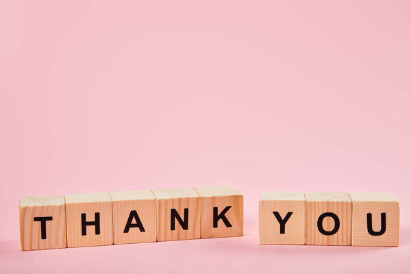 wooden blocks with thank you lettering on pink background with copy space