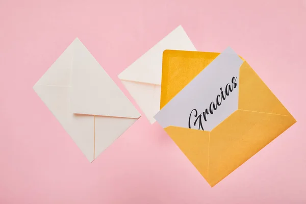 ピンクの背景の文字の近くに白いカードにグラシアスの文字と黄色の明るい封筒 — ストック写真