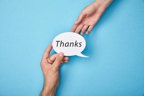 cropped view of man giving white speech bubble with thanks word to woman on blue background