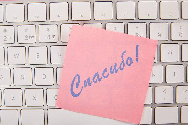 top view of pink sticky note with thankful lettering in Russian language on laptop keyboard 