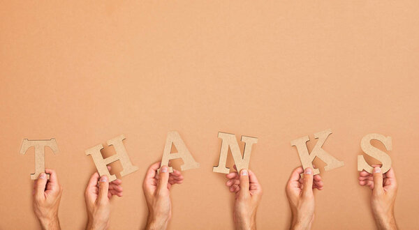 partial view of men holding word thank arranged from paper cut letters on beige background