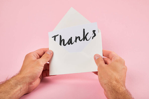 cropped view of man holding envelope and white card with thanks word on pink background