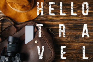 top view of brown leather bag, hat, digital camera and smartphone on wooden table with hello travel illustration clipart