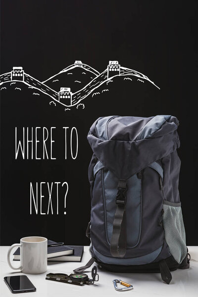 backpack, cup, notebooks, smartphone and trekking equipment isolated on black with where to next question