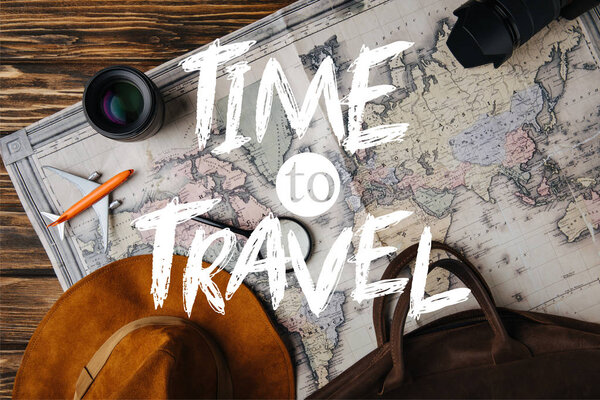 top view of brown leather bag, hat, magnifying glass, model plane, photo camera and lens on map with time to travel illustration