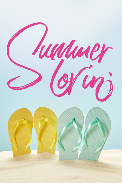 summer yellow and blue flip flops in golden sand isolated on blue with summer lovin lettering
