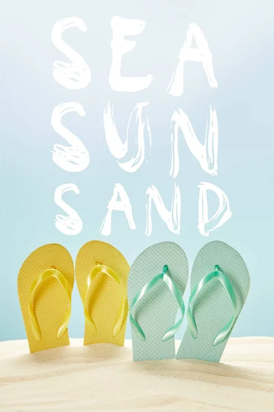 summer yellow and blue flip flops in golden sand isolated on blue with sea, sun and sand lettering