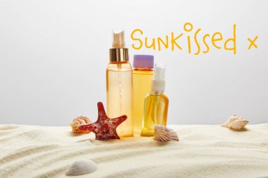 bottles with sunscreen products on sand with starfish on grey background with sun-kissed lettering clipart