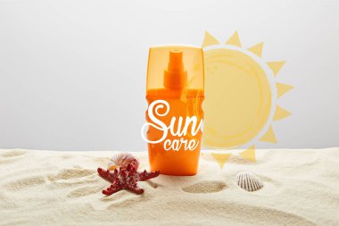 sunscreen in orange bottle on sand with starfish on grey background with sun care lettering clipart