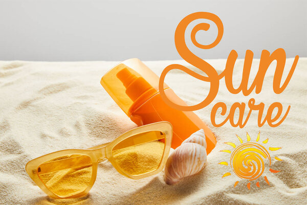 yellow stylish sunglasses and sunscreen in orange bottle on sand with seashell on grey background with sun care lettering