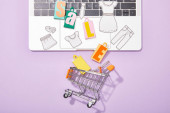 top view of small paper bags with sale lettering and paper cut of clothes on laptop falling in toy shopping cart on violet 