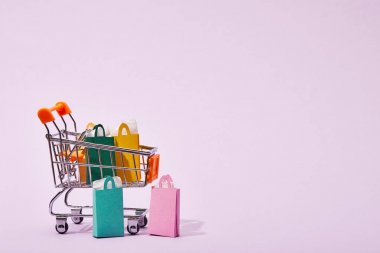 few shopping bags near toy decorative cart with colorful paper bags on violet  clipart