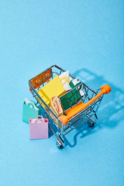 mavi arka plan üzerinde birkaç alışveriş torbaları yakınında renkli kağıt torbalar ile oyuncak sepeti