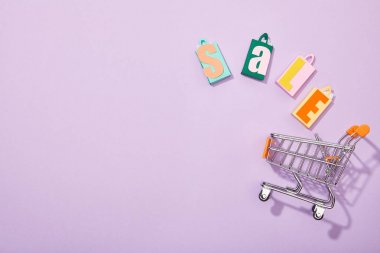 menekşe üzerinde oyuncak sepetine düşen satış yazıt ile renkli alışveriş çantaları üst görünümü 