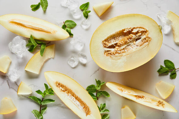 top view of cut delicious seasonal melon on marble surface with mint and ice