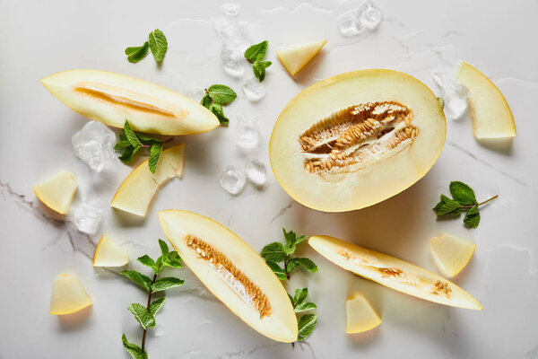 top view of cut tasty melon on marble surface with mint and ice