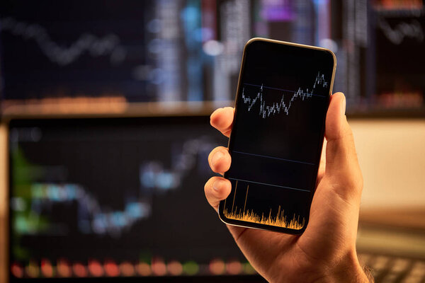 обрезанный вид человека, держащего смартфон с графиками и диаграммами
 