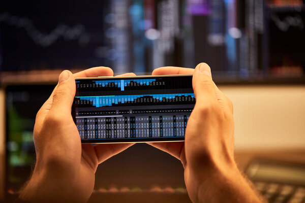 обрезанный вид человека, держащего смартфон с графиками и диаграммами
 