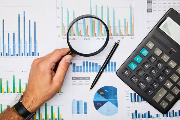 cropped view of man holding magnifying glass and looking at papers