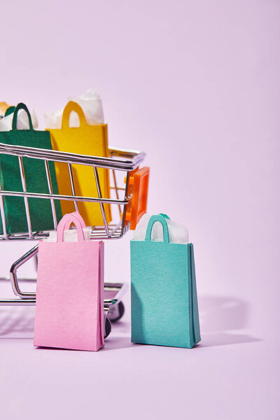 few shopping bags near toy cart with colorful paper bags on violet background