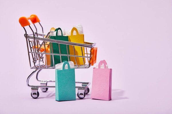 toy cart with colorful paper bags near few shopping bags on violet background