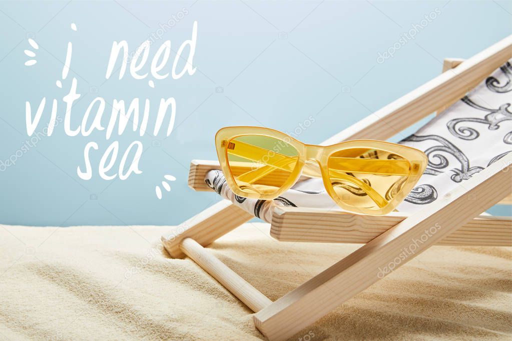 yellow stylish sunglasses on deck chair on sand and blue background with I need vitamin sea lettering