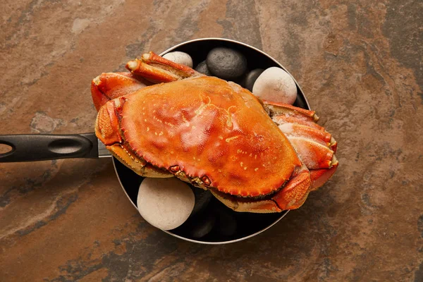 在纹理表面的煎锅中用黑石头做实壳的生蟹的顶视图 — 图库照片