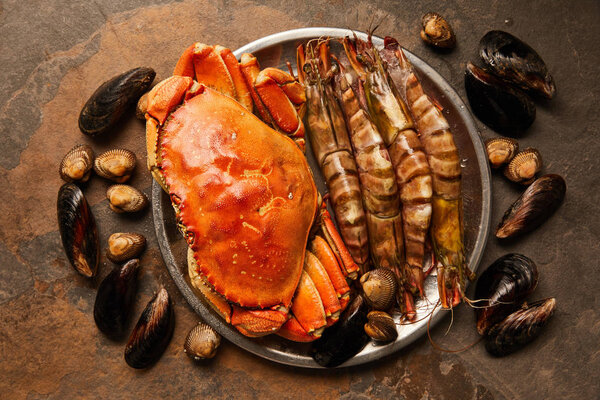 top view of raw crab and shellfish in bowl near scattered cockles and mussels on textured surface 