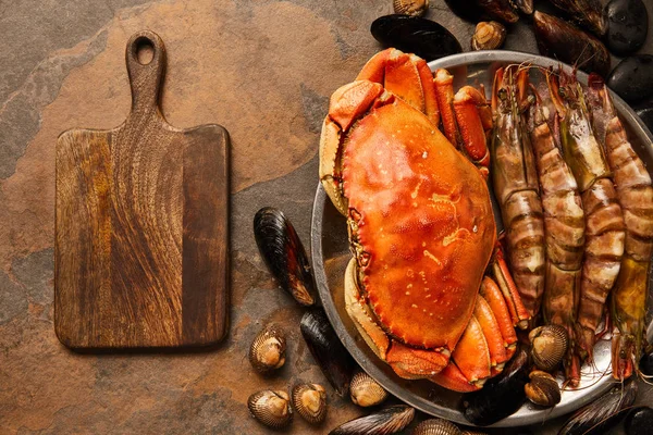 在纹理表面的木切板附近的碗中未煮熟的螃蟹 公鸡和贝类的顶视图 — 图库照片