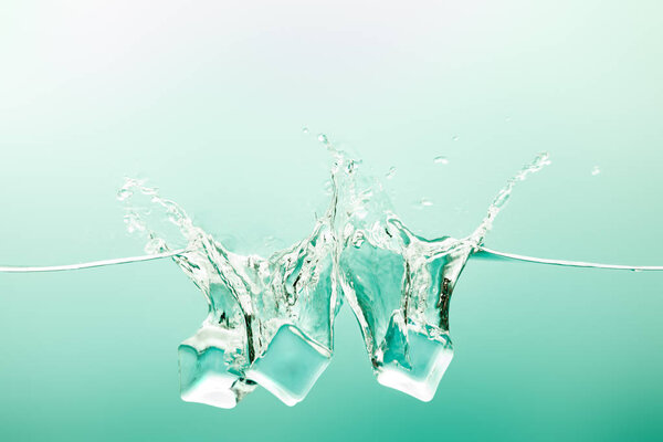 transparent pure water with splash and ice cubes on green background