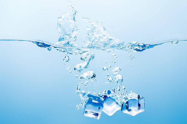 Чистая вода с брызгами, пузырьками и кубиками льда на синем фоне
