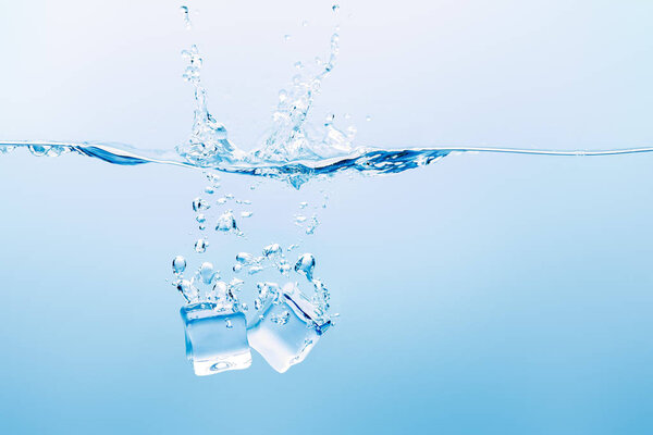 transparent water with splash, bubbles and ice cubes on blue background