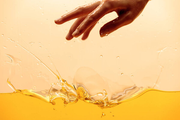 cropped view of hand and yellow bright splashing liquid isolated on yellow