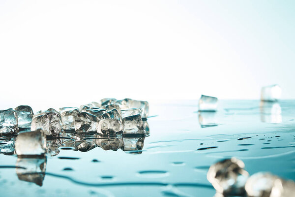 куча прозрачных талых кубиков льда с лужами воды на изумрудном и белом фоне
